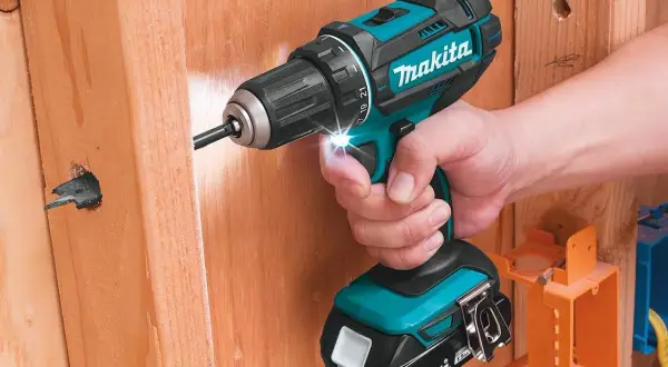 Une perceuse Makita d'origine, tenue par une main, perce un trou dans du bois. L'outil est puissant et fiable.