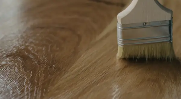 Application d'un vernis ou huile pour bois avec un pinceau sur une surface en bois.