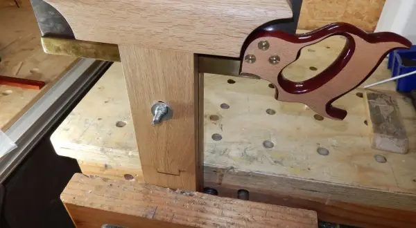 Un guide en bois et laiton aide à comment affûter une lame de banc de scie. La lame est tenue dans un étau.