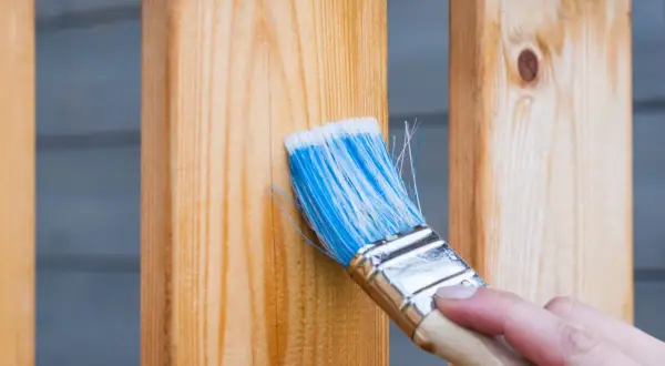 Maintenir le bois avec une lasure ou un vernis : une main applique un produit sur des lattes de bois.