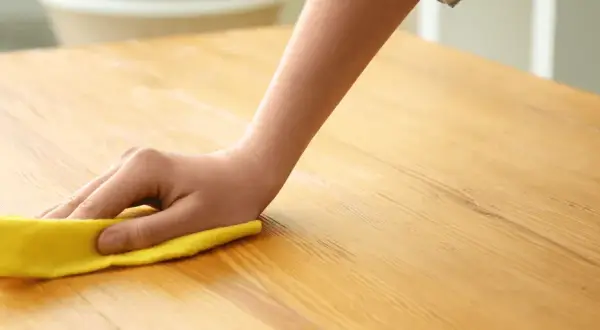 Main d'enfant nettoyant une table en bois avec un chiffon jaune. Apprenez comment nettoyer une table en bois pour un éclat parfait.