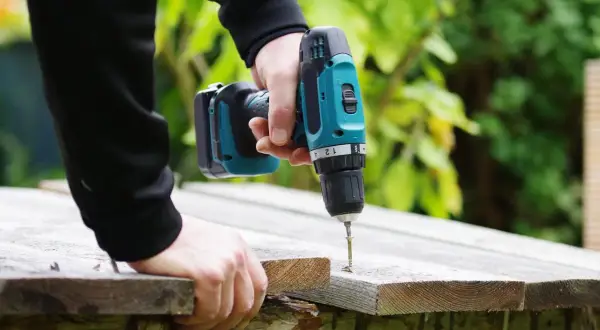Main tenant une perceuse sans fil, il visse une planche de bois. La puissance perceuse permet de réaliser des travaux de bricolage facilement.