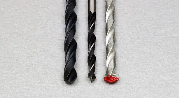 Trois forets de tailles différentes, dont un avec une pointe rouge, prêts à percer un chemin à travers un matériau, comme un foret dans un foret.