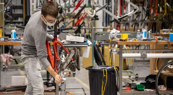 Un ouvrier assemble un vélo rouge, peut-être une création de la marque Korman, dans un atelier rempli de cadres.