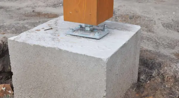 Un poteau en bois est fixé sur un plot béton à enterrer, prêt pour une construction solide.