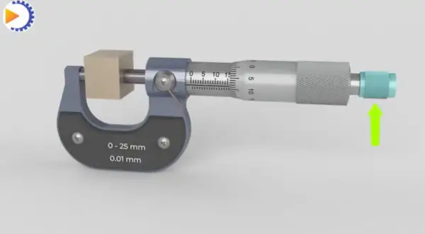 Un micromètre mesure un petit cube de bois. L'outil de précision affiche une mesure de 0 à 25 mm avec une précision de 0,01 mm.
