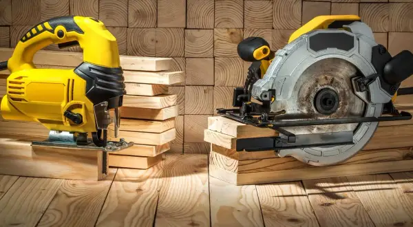 Scie sauteuse jaune et scie circulaire argentée, prêtes à découper du bois. La différence entre ces outils est claire pour tout bricoleur.