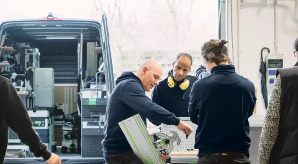 Des artisans discutent d'un outil Festool, l'origine de leur savoir-faire, devant un fourgon aménagé.