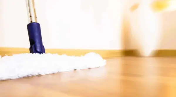 Une serpillère blanche et moelleuse nettoie un parquet brillant. La lumière douce éclaire la scène, créant une ambiance chaleureuse.