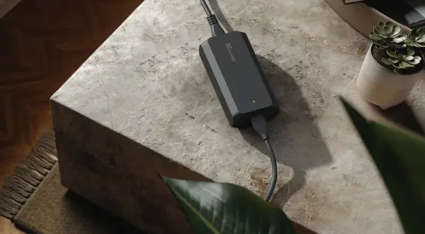Chargeur noir avec une lumière verte allumée, posé sur une table en pierre. La question "peut on charger une batterie 4ah avec un chargeur 2ah" est soulevée par cet appareil.