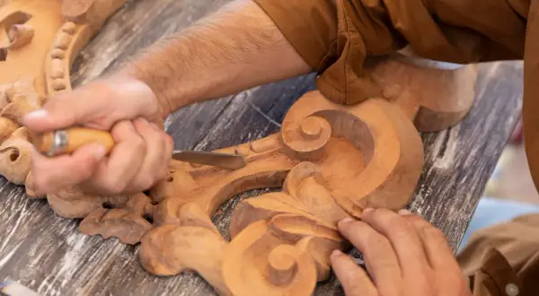 Un artisan utilise un ciseau pour sculpter le bois, créant des volutes complexes sur une pièce ornementale.