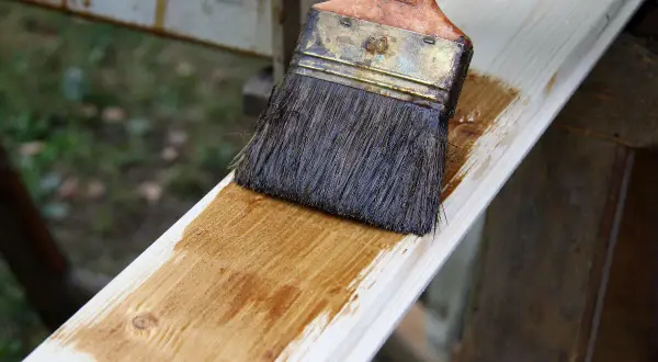Application d'une lasure effet bois blanchi sur une planche de bois clair. Le pinceau dépose une fine couche de produit.