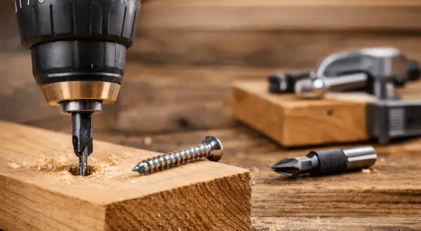 Apprenez comment utiliser une perceuse pour visser dans le bois. Une mèche est dans le bois, une vis à côté.