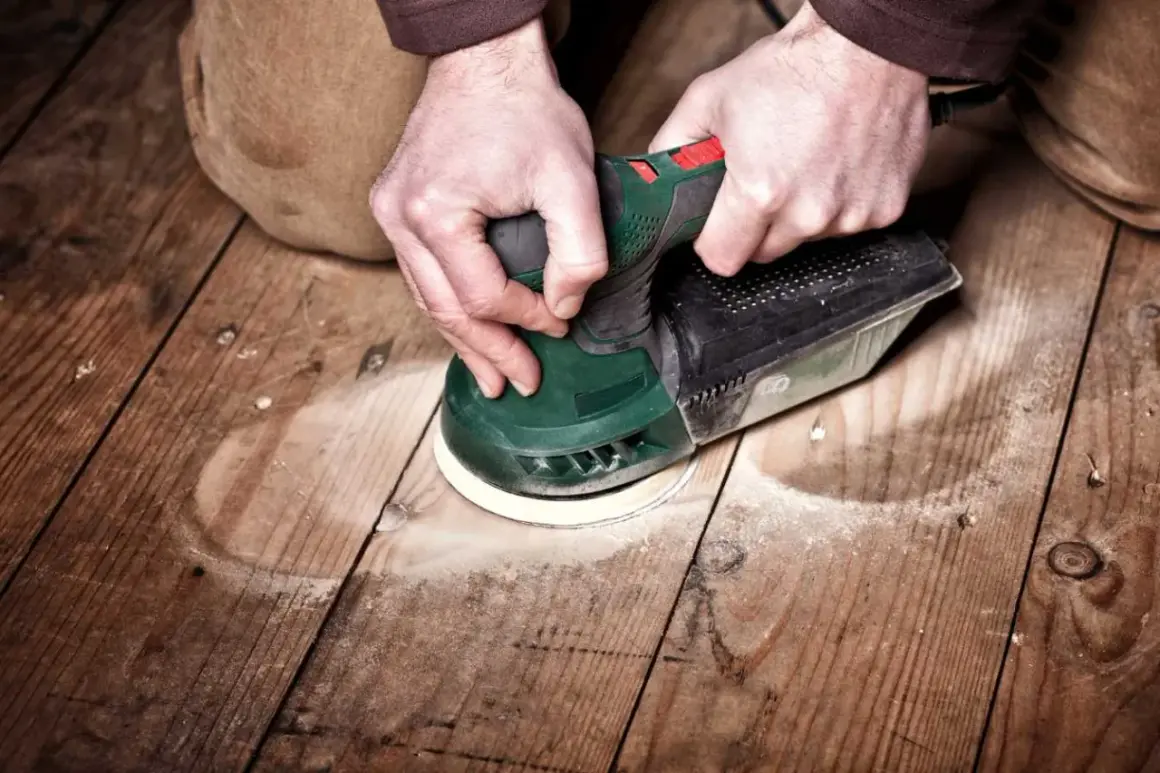 Mains tenant une ponceuse pour le ponçage du parquet. La poussière vole autour de l'outil pendant le travail.
