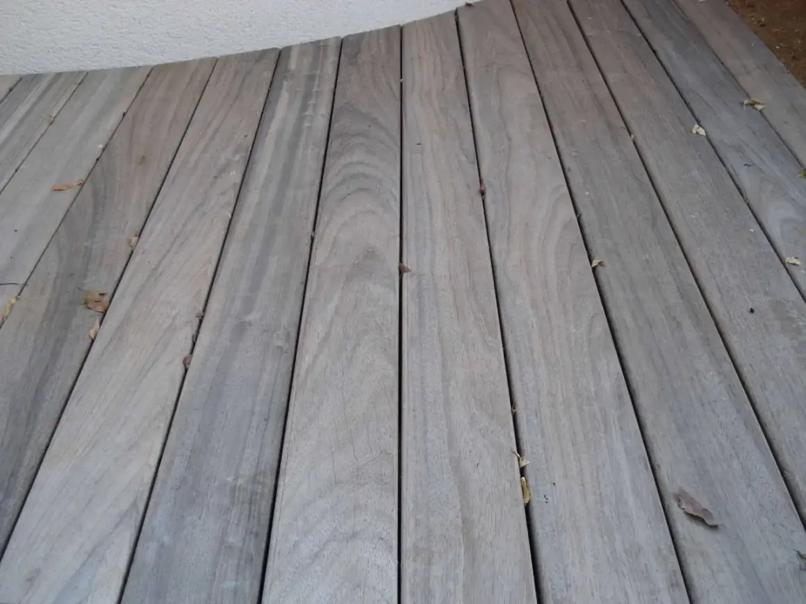 Planches de bois grisé, patinées par le temps, formant une terrasse. Quelques feuilles mortes parsèment le sol.
