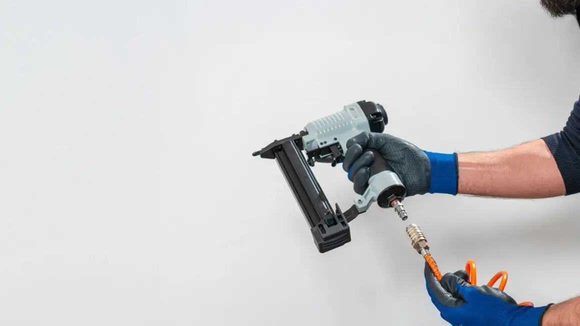 Main d'un bricoleur connectant un tuyau à un pistolet à clous pneumatique, un outil essentiel pour tout projet de menuiserie.