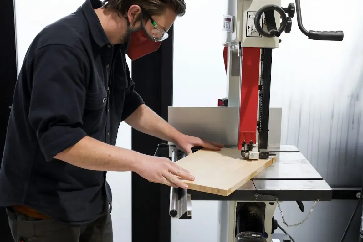 Un artisan utilise une scie à ruban, un des outils pour couper le bois, pour façonner une planche.