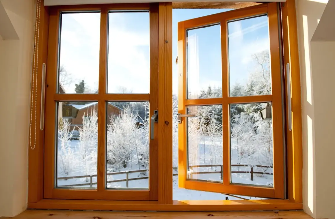 Une fenêtre en bois, prête à être poncée, s'ouvre sur un paysage hivernal enneigé.