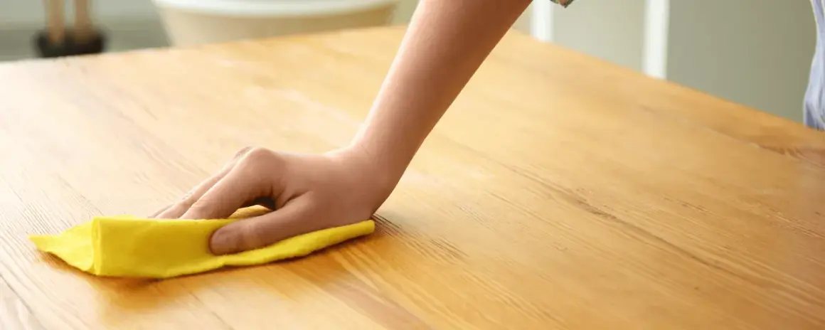 Main d'enfant nettoyant une table en bois avec un chiffon jaune. Apprenez comment nettoyer une table en bois pour un éclat parfait.