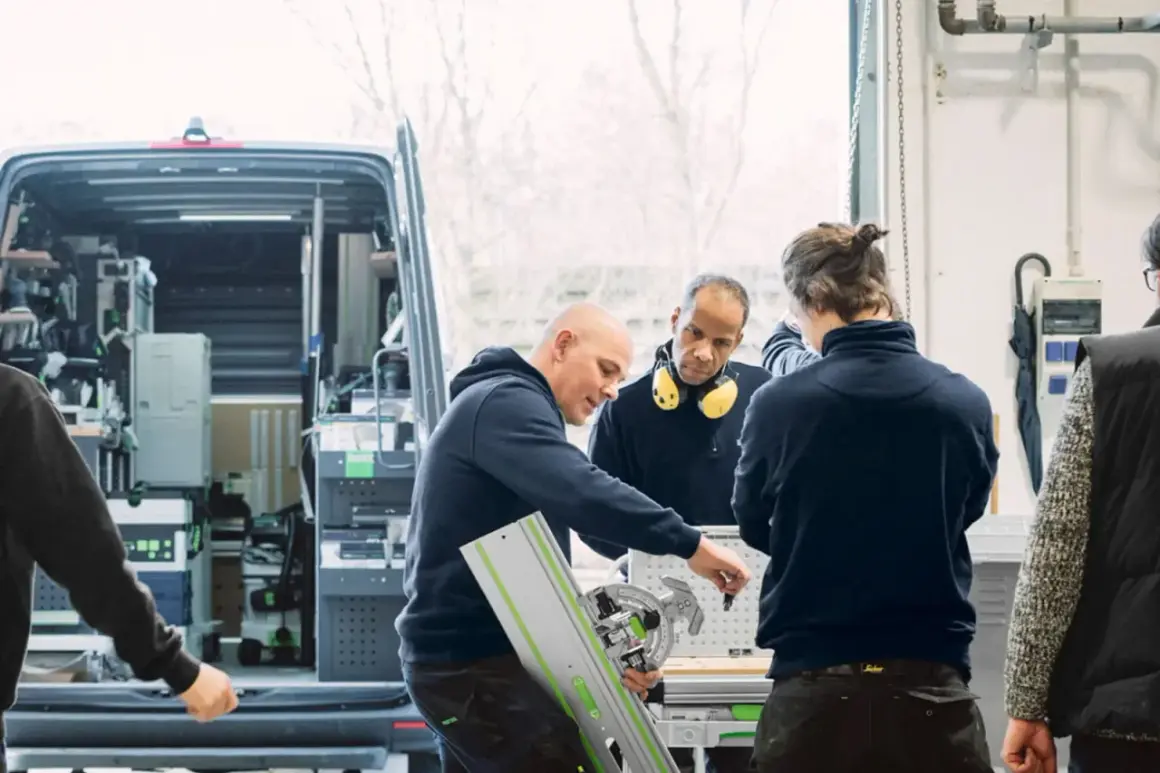 Des artisans discutent d'un outil Festool, l'origine de leur savoir-faire, devant un fourgon aménagé.