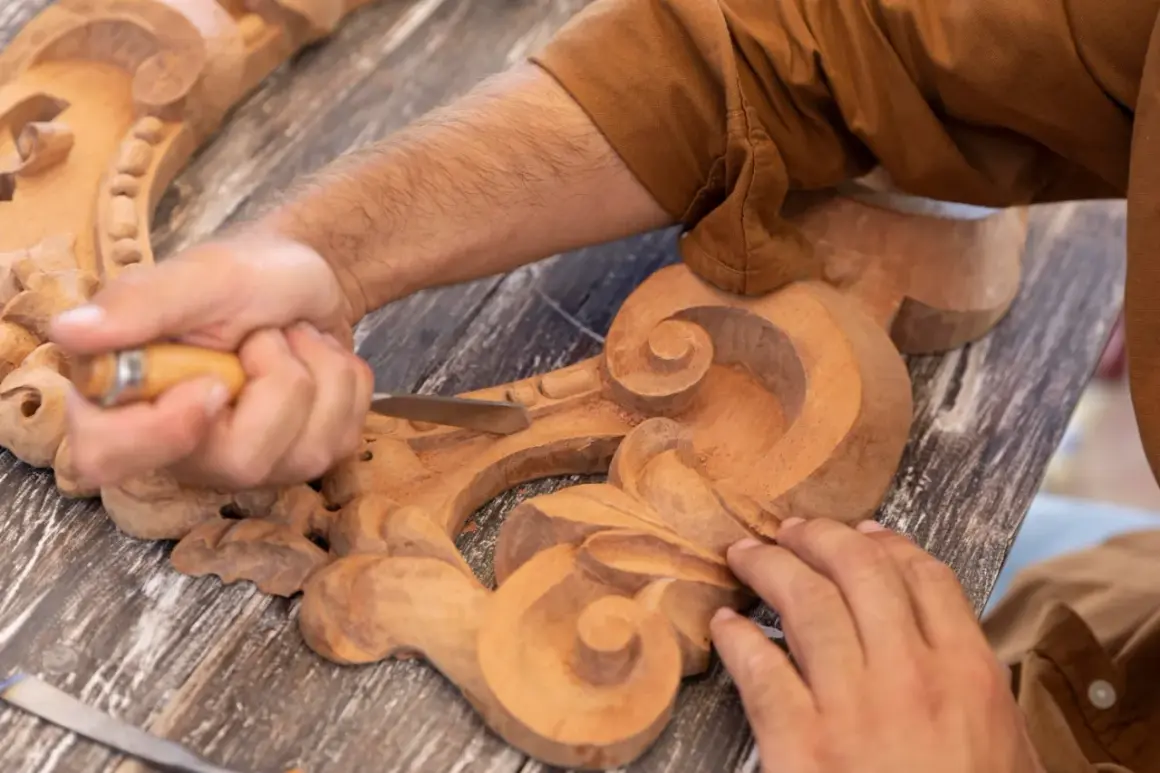 Un artisan utilise un ciseau pour sculpter le bois, créant des volutes complexes sur une pièce ornementale.