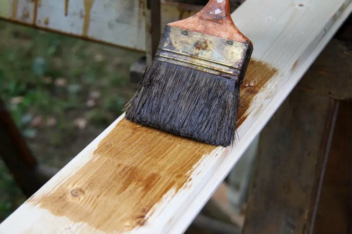 Application d'une lasure effet bois blanchi sur une planche de bois clair. Le pinceau dépose une fine couche de produit.