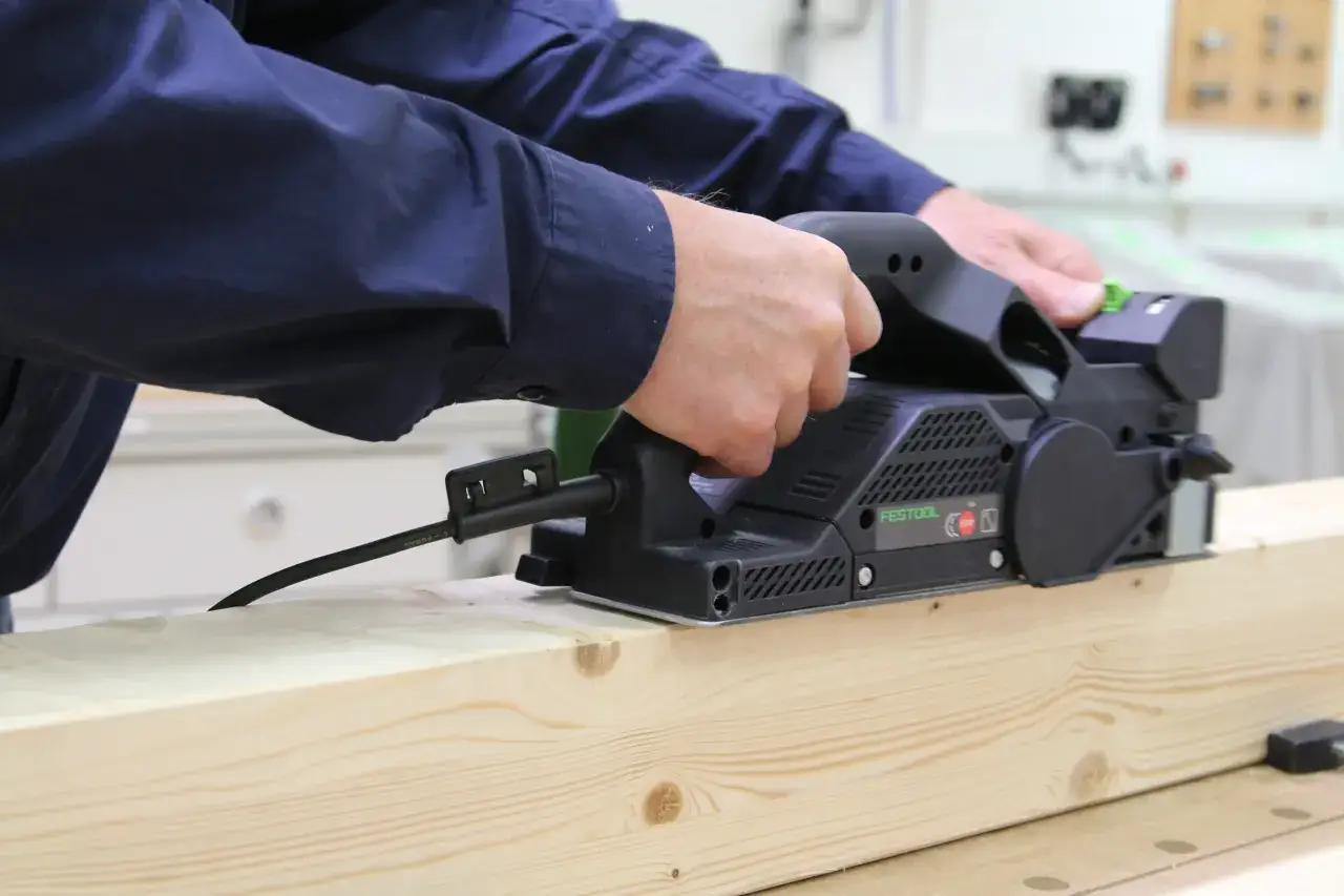 Mains raboteuse Festool en action, lissant une planche de bois avec précision.