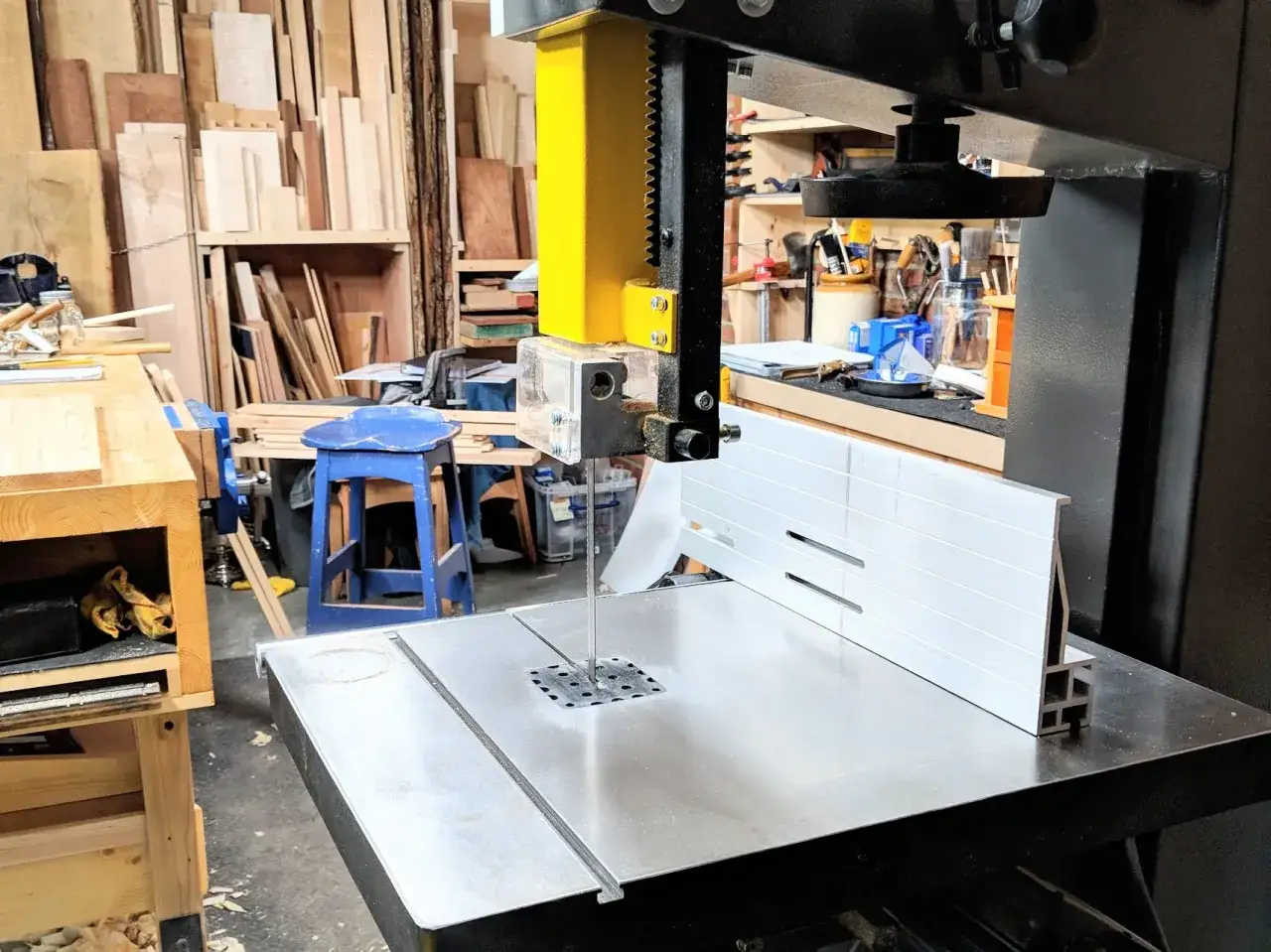Dans un atelier, une scie à ruban est prête à découper du bois. Un marteau repose à proximité, attendant sa tâche.