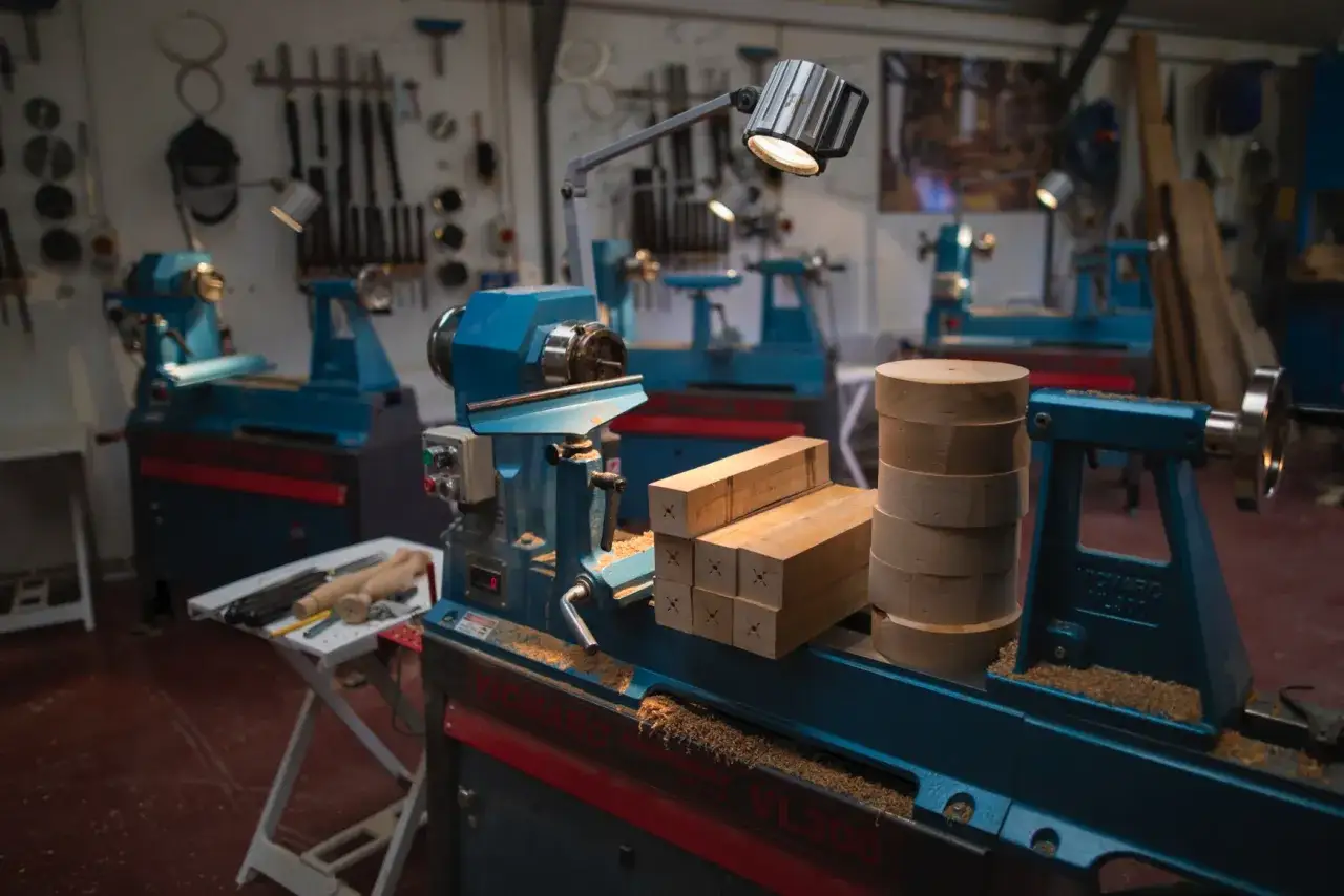 Atelier de menuiserie avec plusieurs tours &agrave; bois d'&eacute;tabli bleus. Des blocs de bois et des pi&egrave;ces cylindriques sont pr&ecirc;ts &agrave; &ecirc;tre travaill&eacute;s.