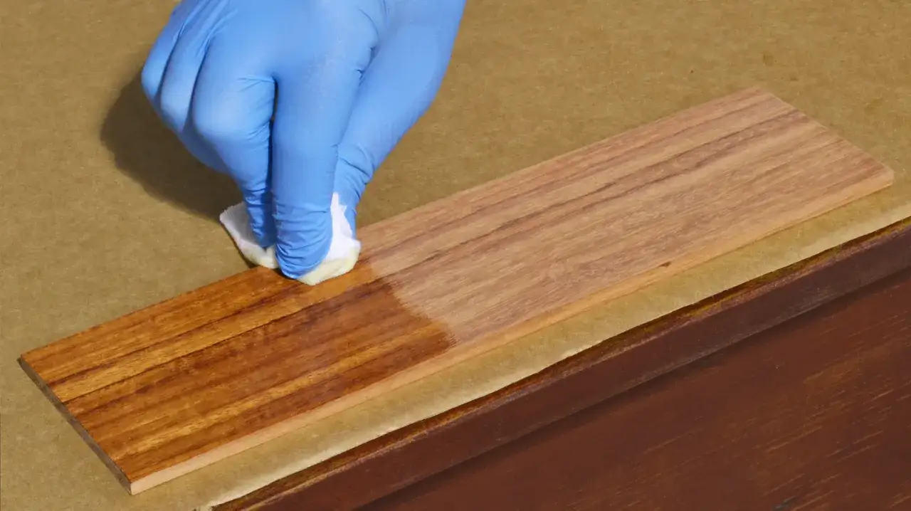 Main tenant une éponge imbibée d'huile de lin bois, protégeant le bois avec un gant bleu.