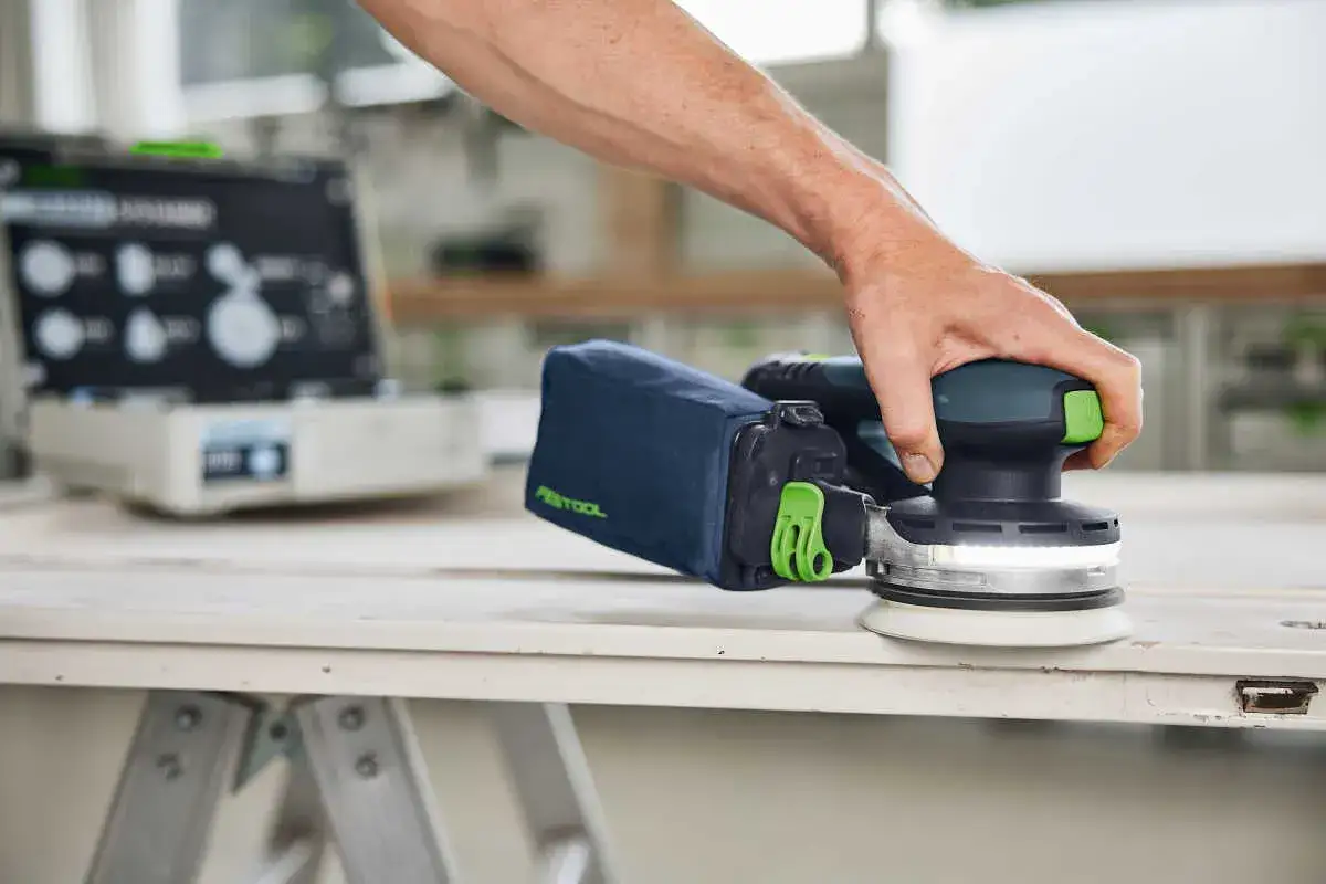 Main d'un artisan utilisant une ponceuse excentrique etsc 125 pour lisser une surface en bois.