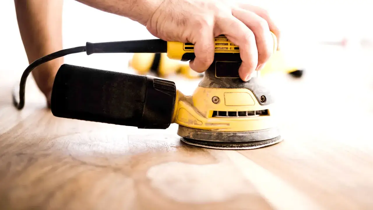 Main d'artisan utilisant une ponceuse orbitale pour le ponçage bois d'un plancher.