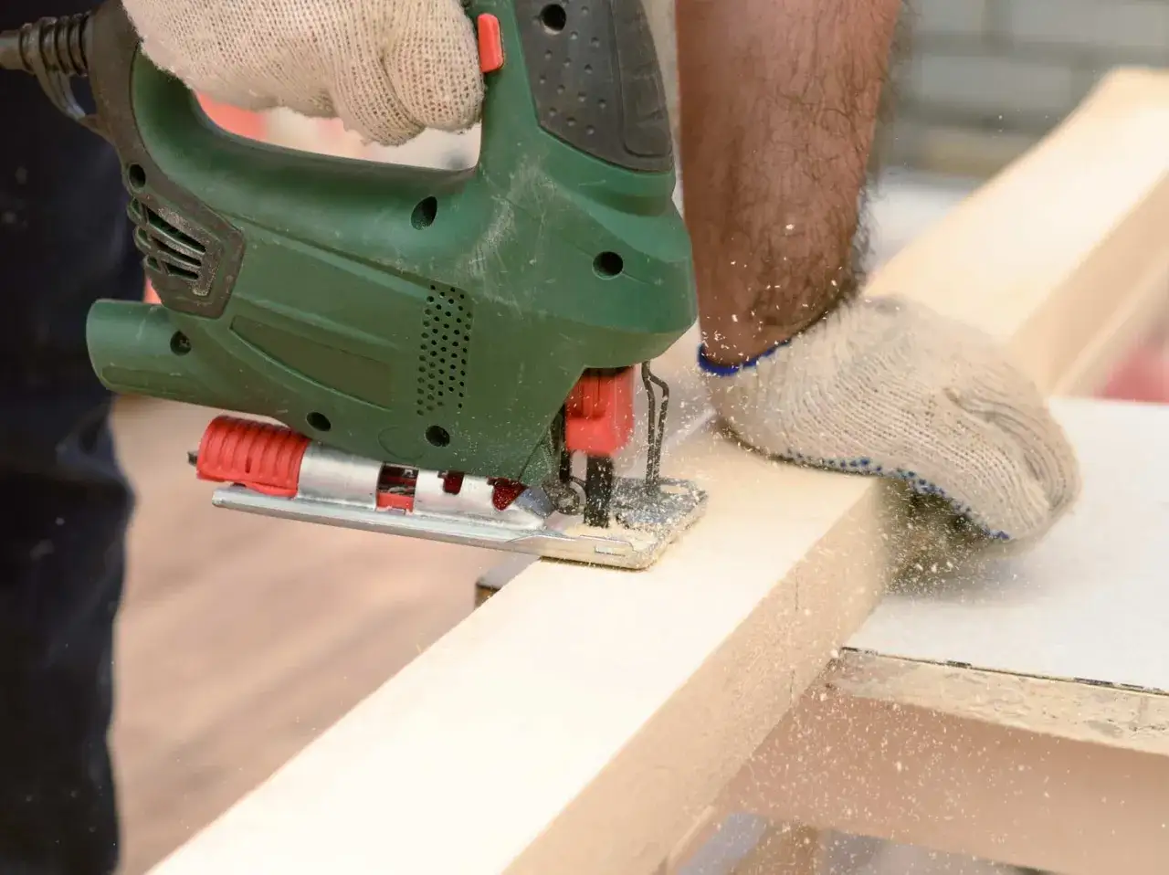 Main d'un bricoleur portant un gant utilise une scie toupie pour découper une planche de bois.