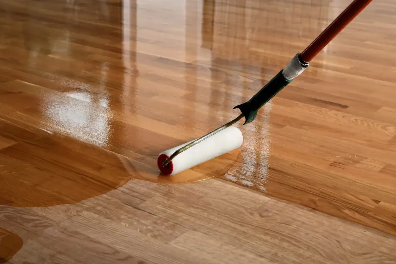 Application d'un vernis brillant sur un parquet en bois. Le rouleau laisse une finition lisse et un fond dur.