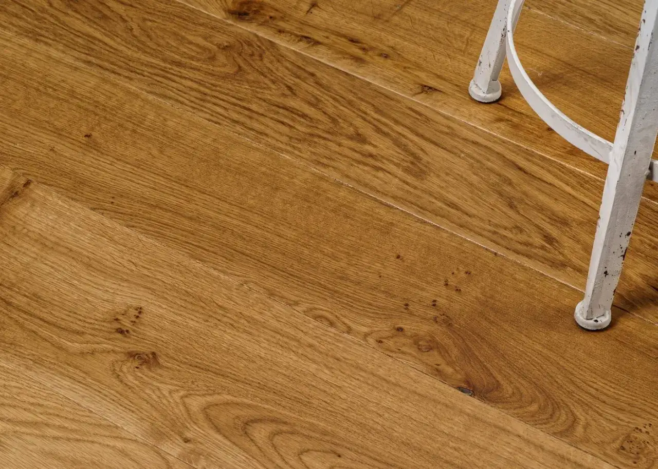 Gros plan sur un parquet huil&eacute; ou cir&eacute; aux teintes chaudes, avec le pied d'une chaise blanche en arri&egrave;re-plan.