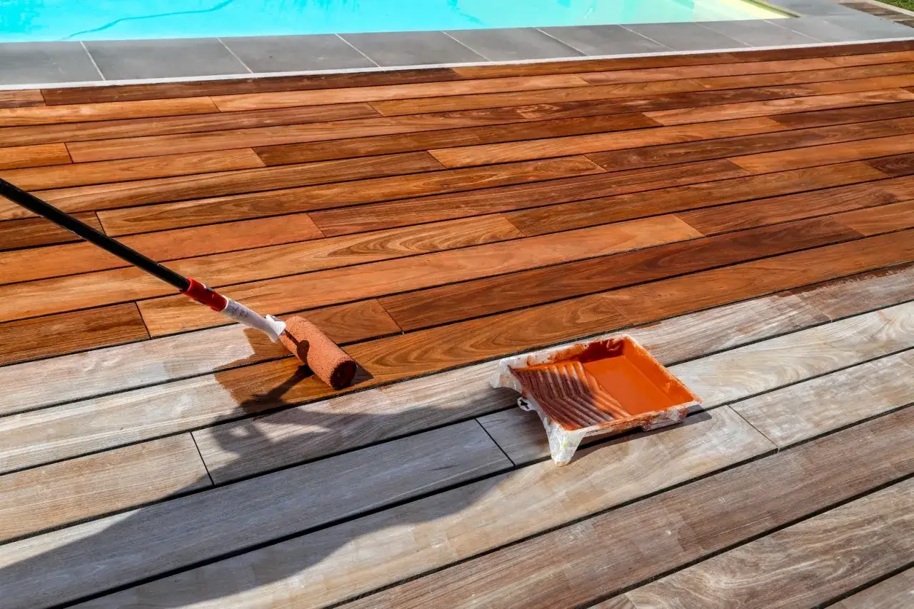 Application d'un produit de traitement bois exotique sur une terrasse en bois, près d'une piscine.