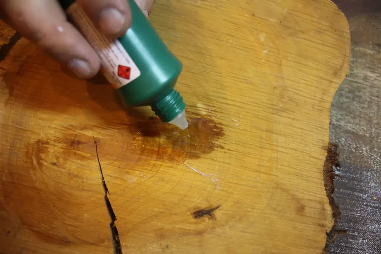 Application d'un produit sur du bois pour comment enlever de la colle sèche. Le liquide se répand sur la surface du bois.