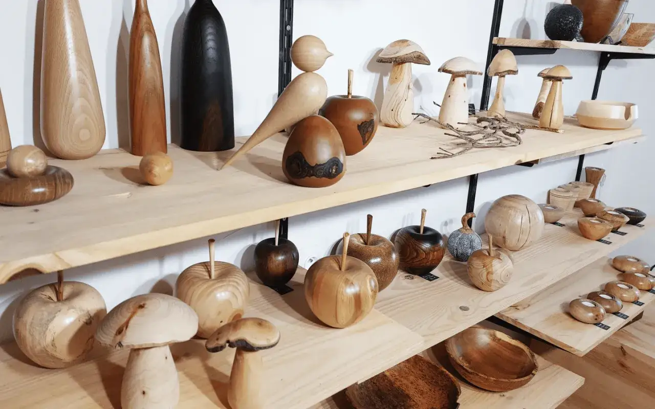 Objets décoratifs en bois, fruits, champignons et oiseaux, issus du tournage sur bois, exposés sur des étagères.