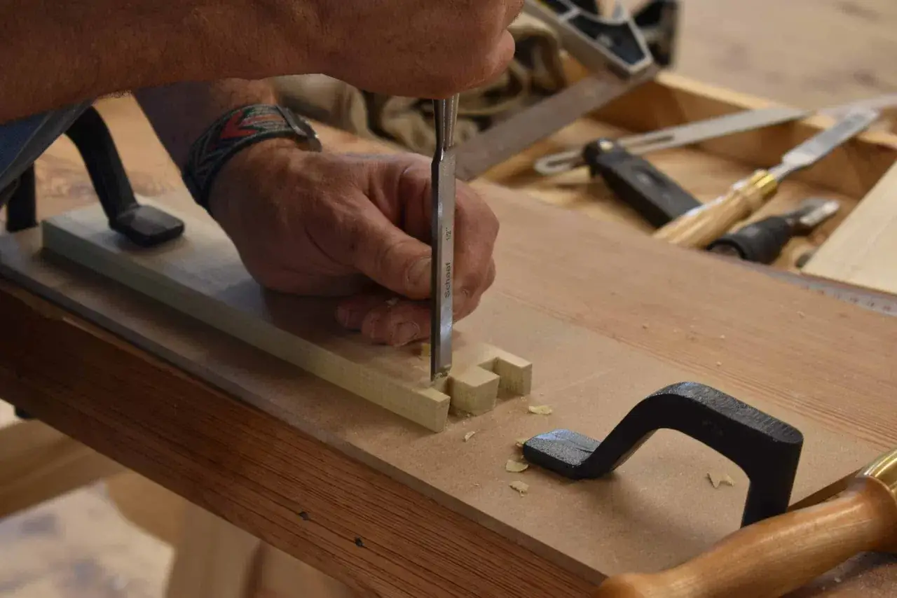 Un artisan façonne un assemblage tenon mortaise avec un ciseau, créant des pièces de bois précises pour un projet de menuiserie.