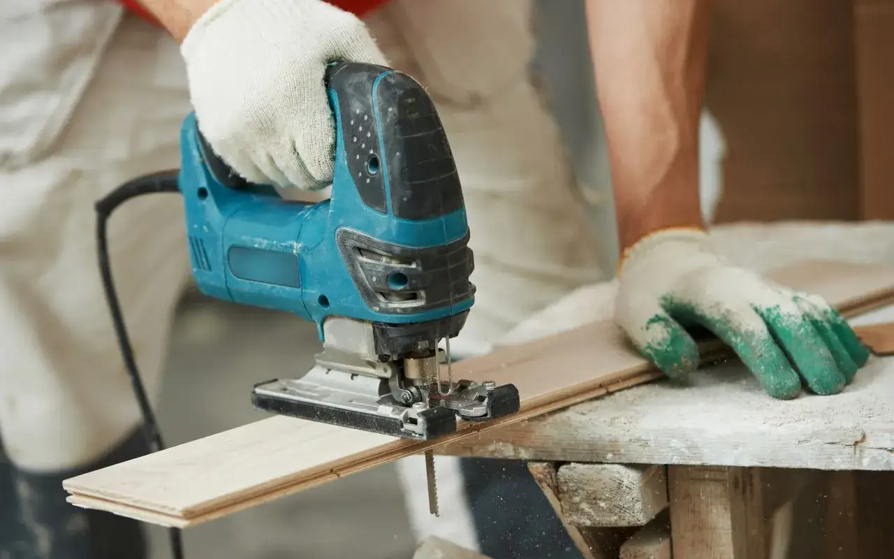 Main tenant utilise une scie sauteuse pour une coupe de travers sur une lame de parquet.