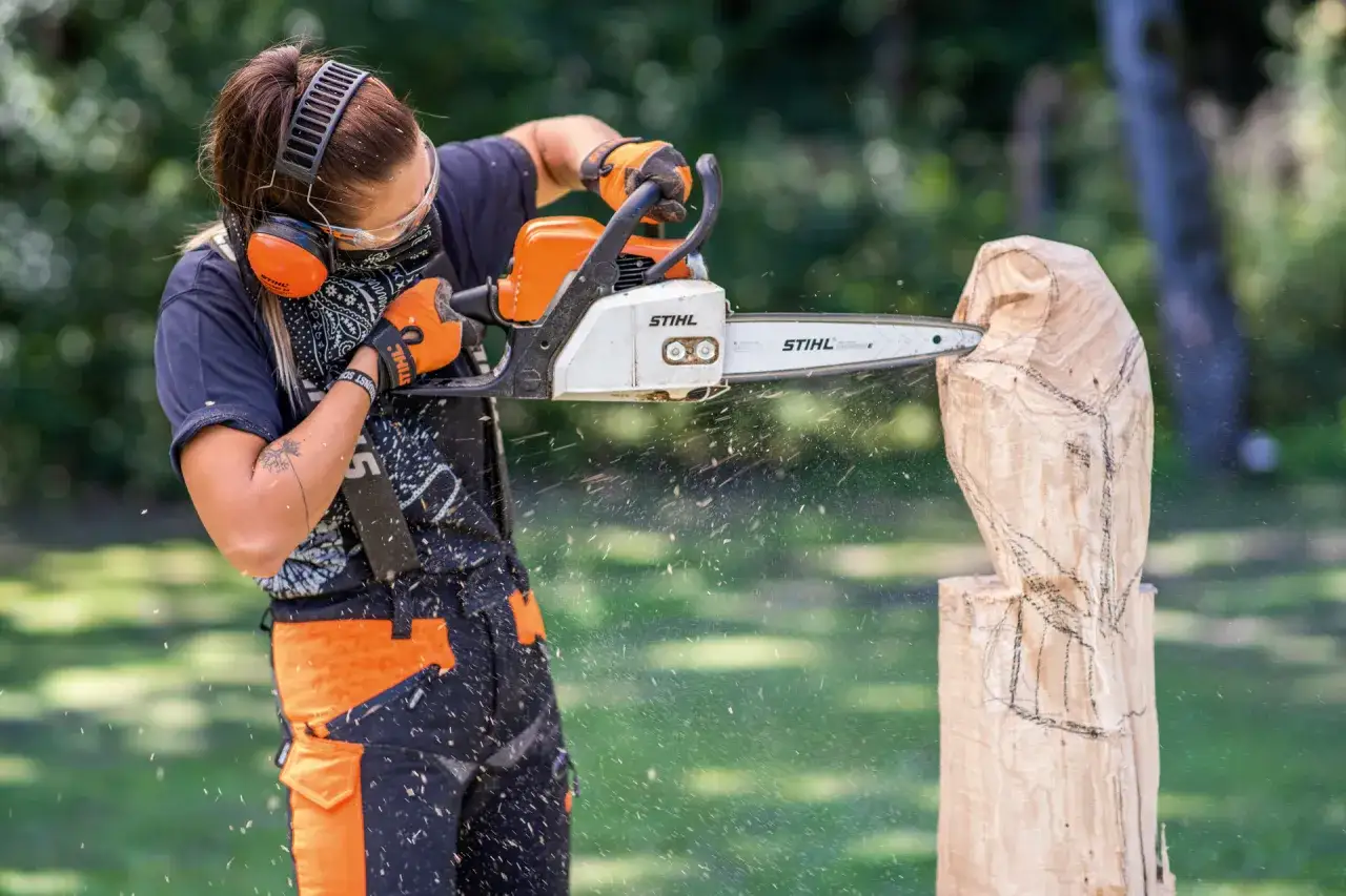 Artiste cr&eacute;ant une sculpture bois tron&ccedil;onneuse facile, des copeaux volent.