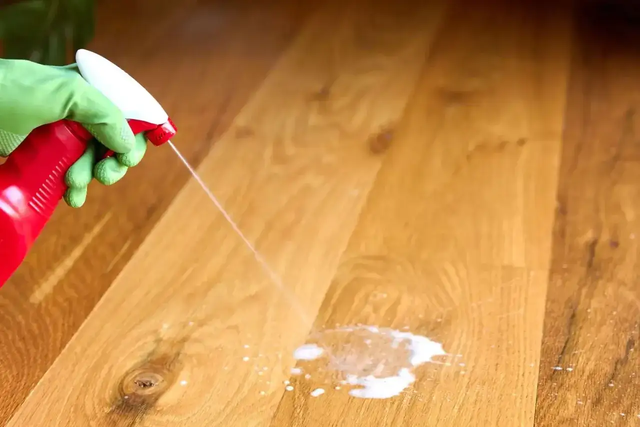 Main verte pulv&eacute;risant un produit pour enlever tache urine sur parquet bois.