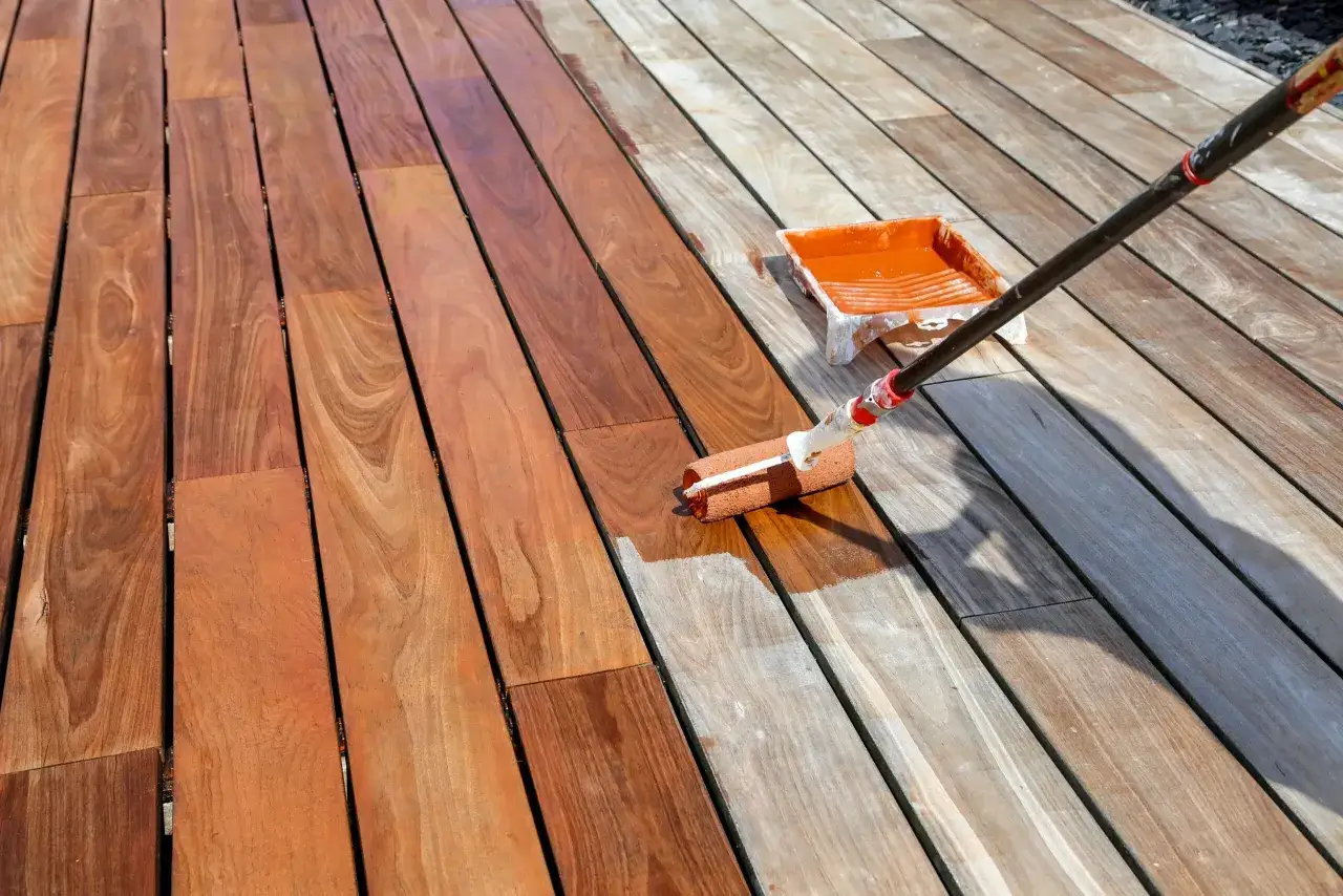 Application d'une première couche de saturateur sur une terrasse en bois. Le rouleau est en action, laissant une teinte orangée. Combien de temps entre 2 couches de saturateur ?