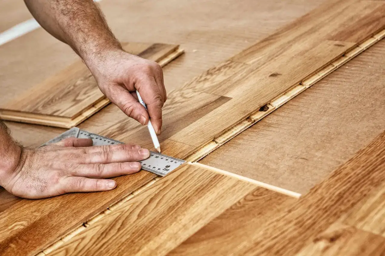 Un artisan mesure une lame de parquet en ch&ecirc;ne pour une pose pr&eacute;cise. La lumi&egrave;re met en valeur le grain du bois.