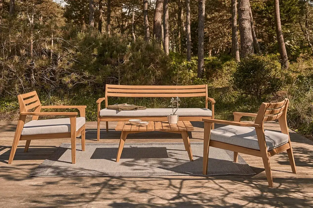 Ensemble de salon ext&eacute;rieur en bois pour table, avec banc et fauteuils, sur une terrasse en bois, entour&eacute; par la nature.