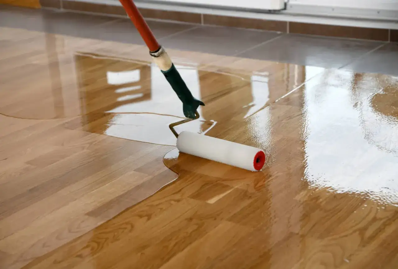 Application d'un vitrificateur sur un parquet lasur&eacute;, le rouleau &eacute;tale le produit pour une finition brillante et protectrice.