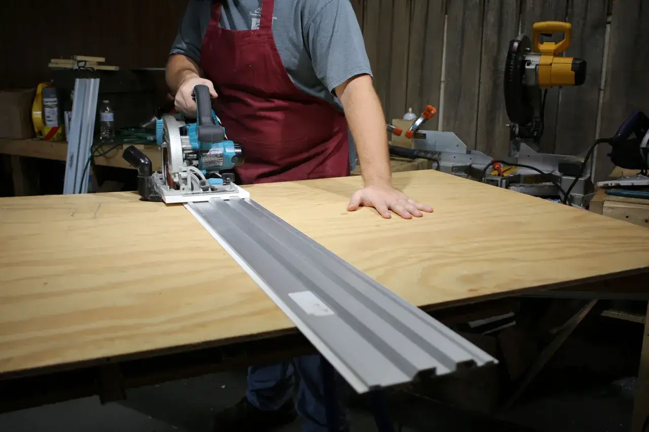 Un artisan utilise une machine scie circulaire sur un rail pour découper une planche de bois.