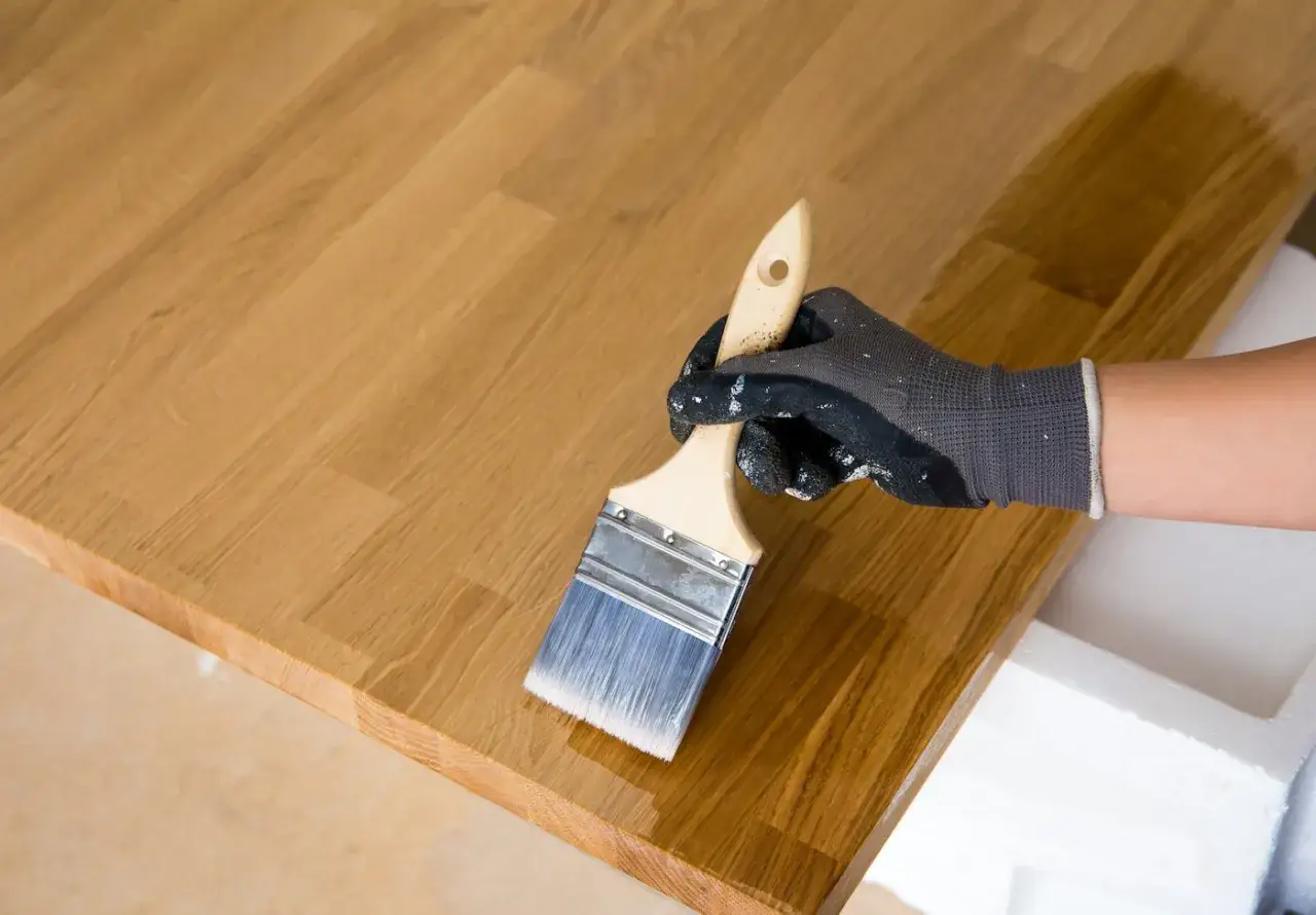 Application d'huile de lin dure naturelle sur un plateau en bois avec un pinceau. Le bois prend une belle teinte dorée.