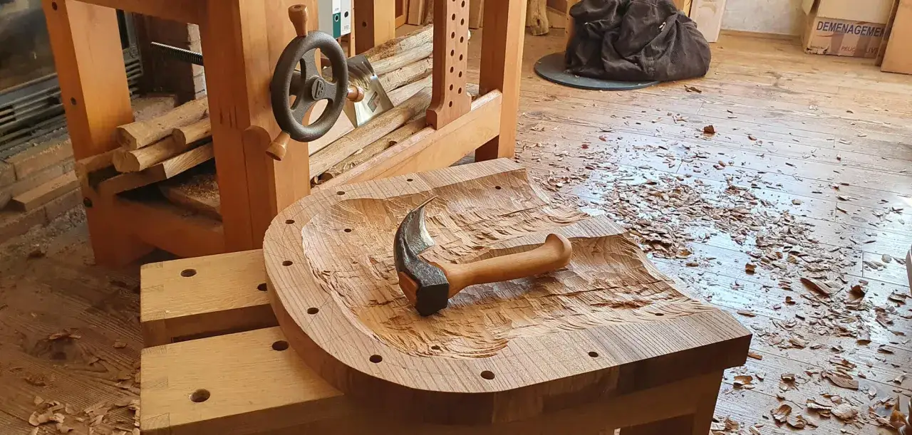 Un marteau repose sur une pièce de bois sculptée, entourée de copeaux. Le materiel ebeniste est prêt pour la suite du travail.