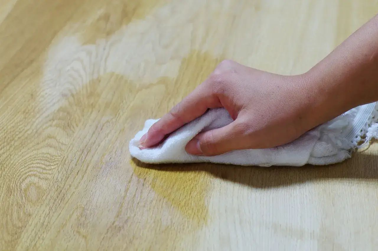 Main d'une personne passant un chiffon blanc sur un parquet en bois pour le nettoyer.